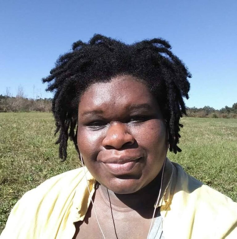 A woman with dreadlocks standing in a field.