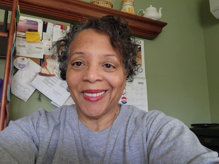 A woman with curly hair smiling in front of a desk.