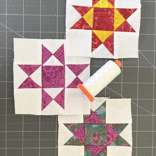 Three quilt blocks with a spool of thread next to them.