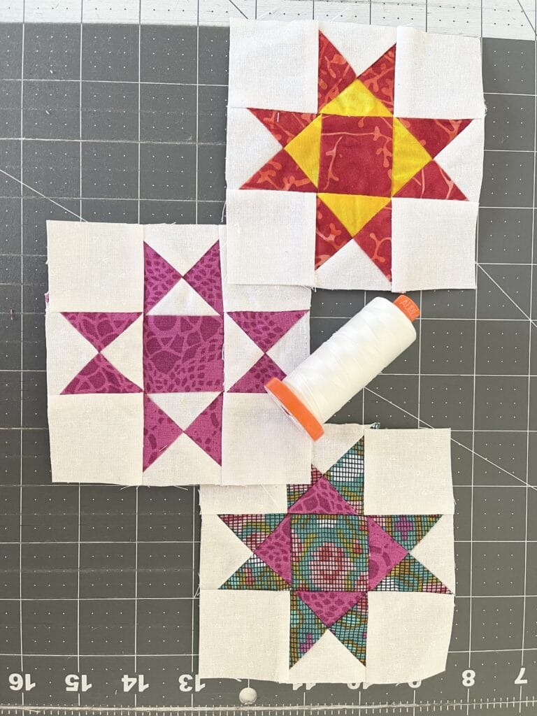Three quilt blocks with a spool of thread next to them.
