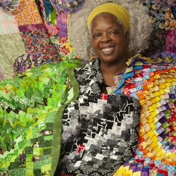 A woman sitting in front of several different colored blankets.