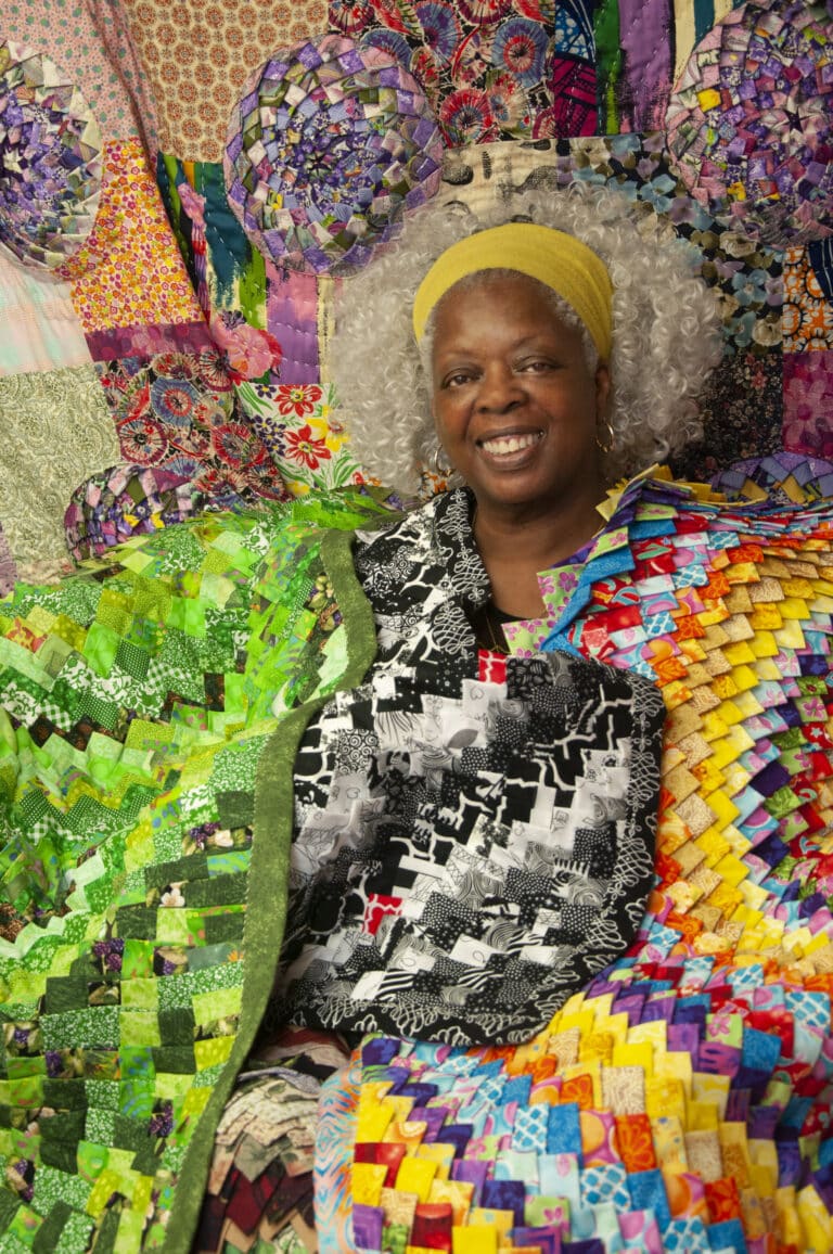 A woman sitting in front of several different colored blankets.