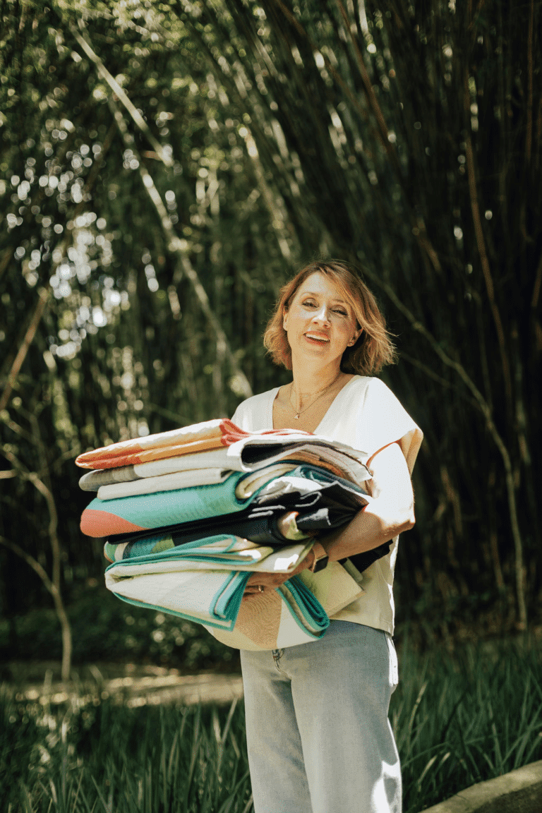 A woman holding a stack of fabric in the woods.