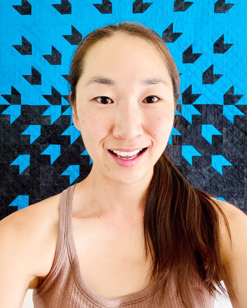 A woman smiling in front of a blue and black quilt.