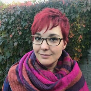 A woman with red hair wearing glasses and a scarf.