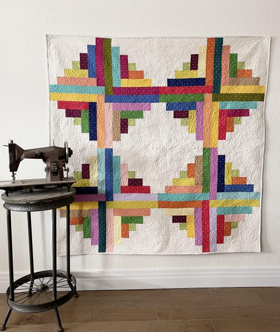A colorful quilt hanging on a wall next to a sewing machine.