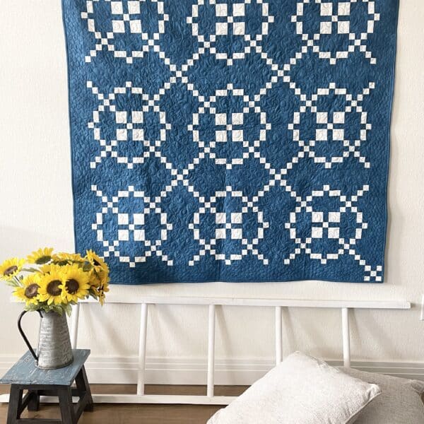 A blue quilt hanging on a wall next to a vase of sunflowers.
