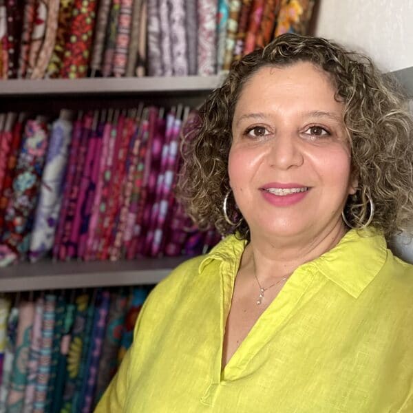 A woman in a yellow shirt standing in front of a shelf full of fabric.