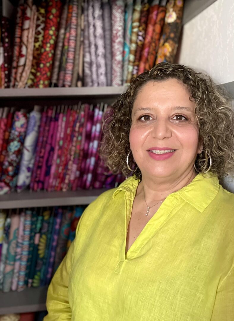 A woman in a yellow shirt standing in front of a shelf full of fabric.