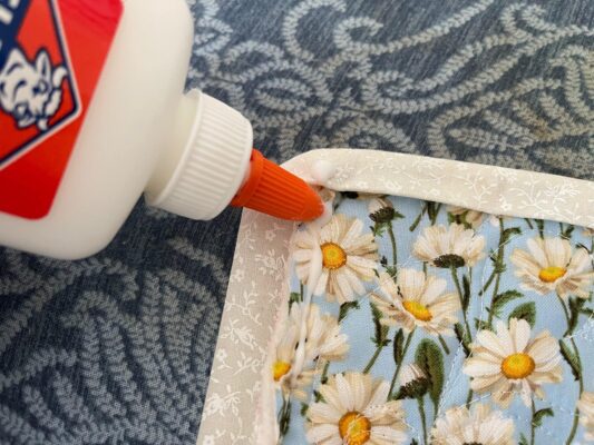 A person is using an orange glue to patch the edge of a flower print fabric.