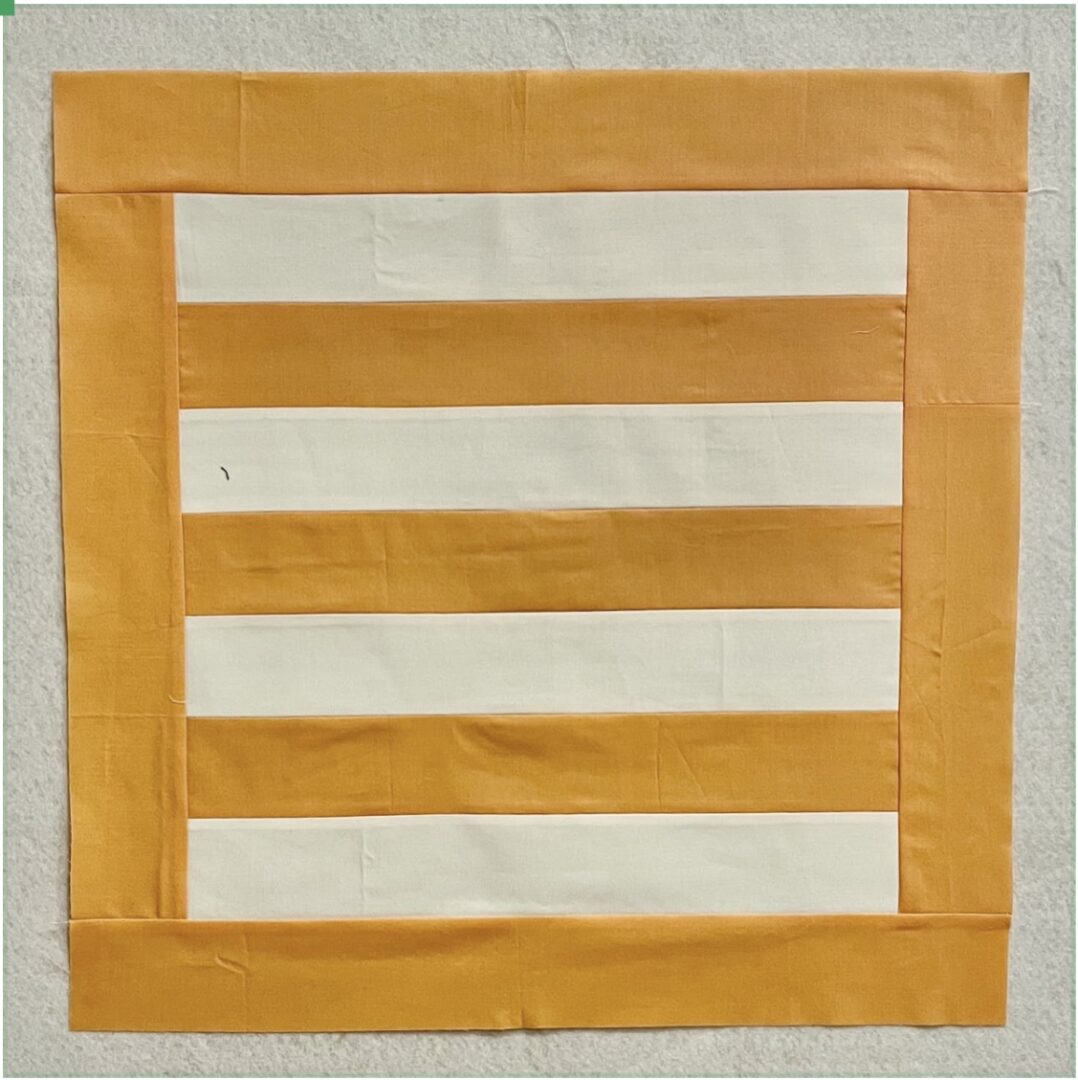 A yellow and white striped quilt block on a piece of paper.