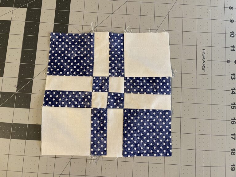 A blue and white quilt block on a cutting mat.