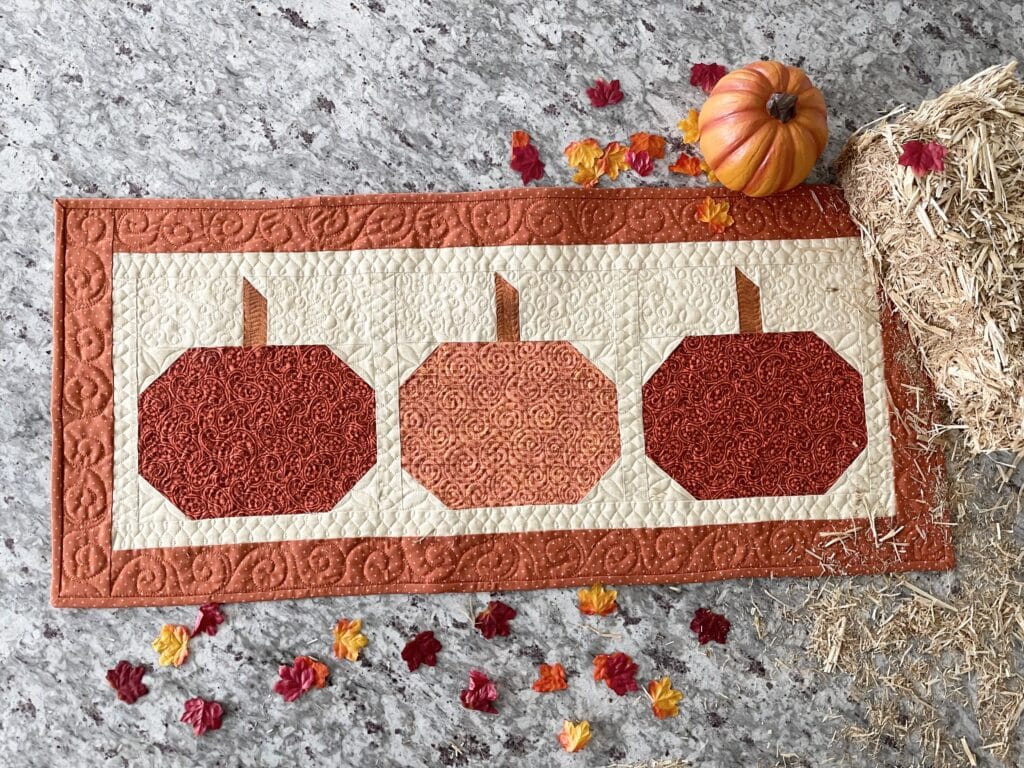 A table runner with three pumpkins on it.