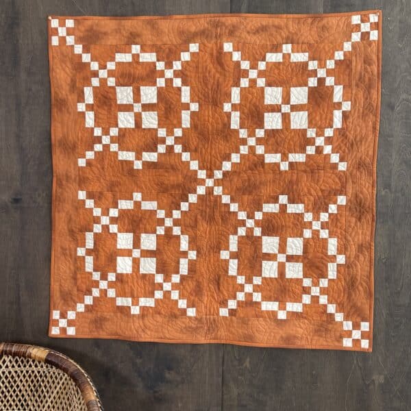 An orange and white quilt hanging on a wooden table.