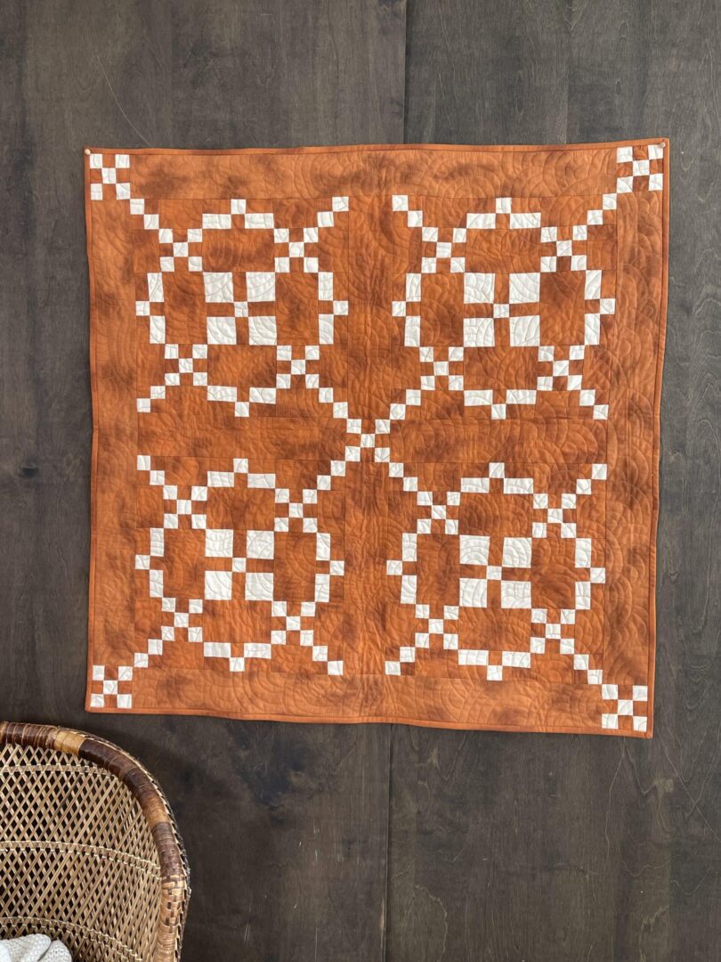 An orange and white quilt hanging on a wooden table.