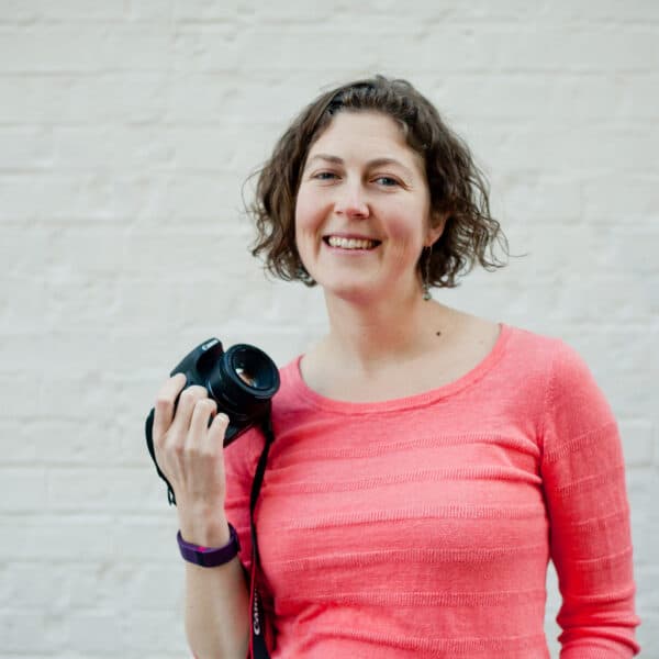 A woman holding a camera in front of a brick wall.