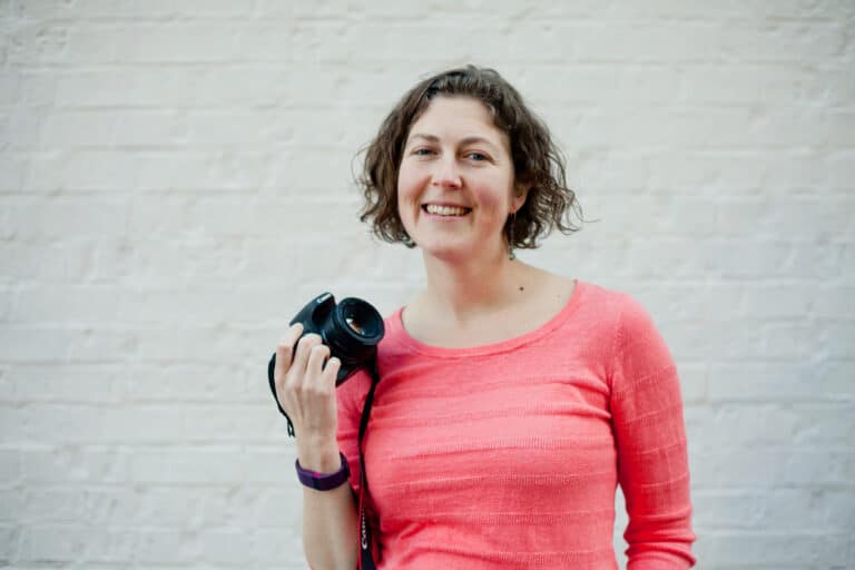 A woman holding a camera in front of a brick wall.