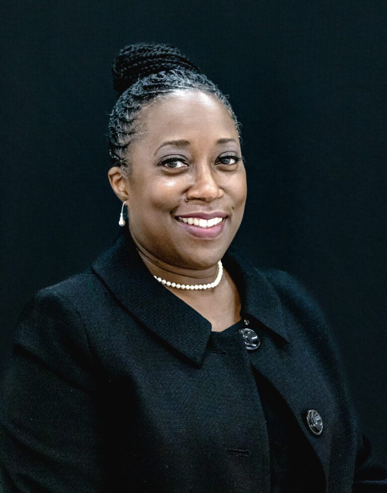 A black woman in a business suit smiles for the camera.