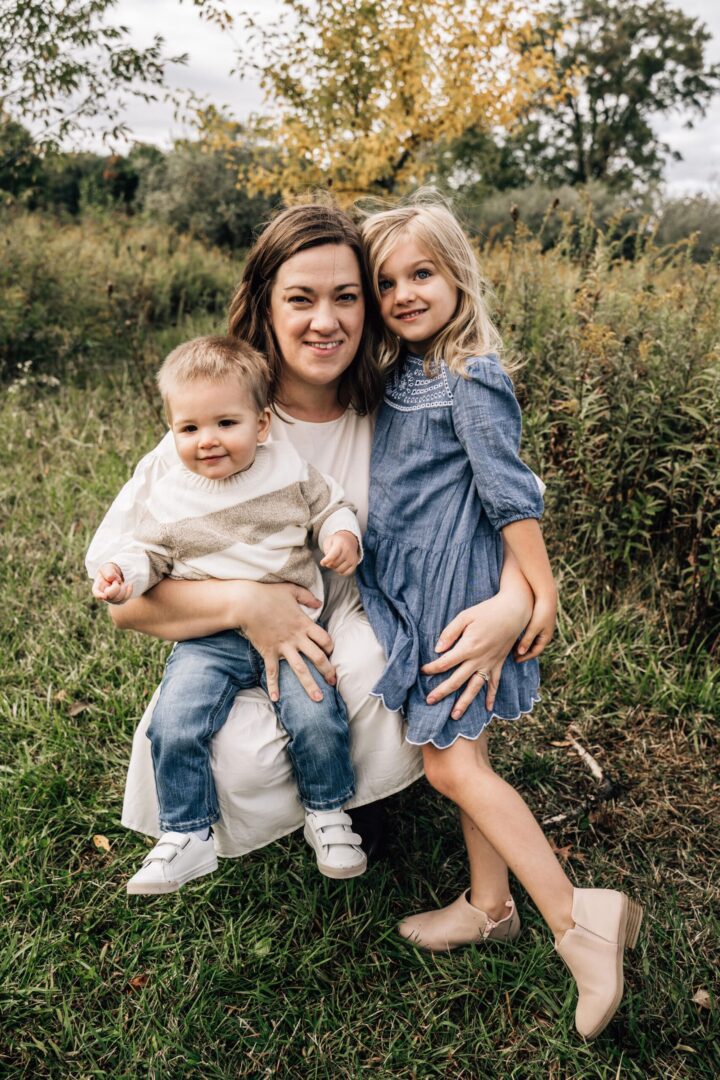 A woman poses with her two children in a field.