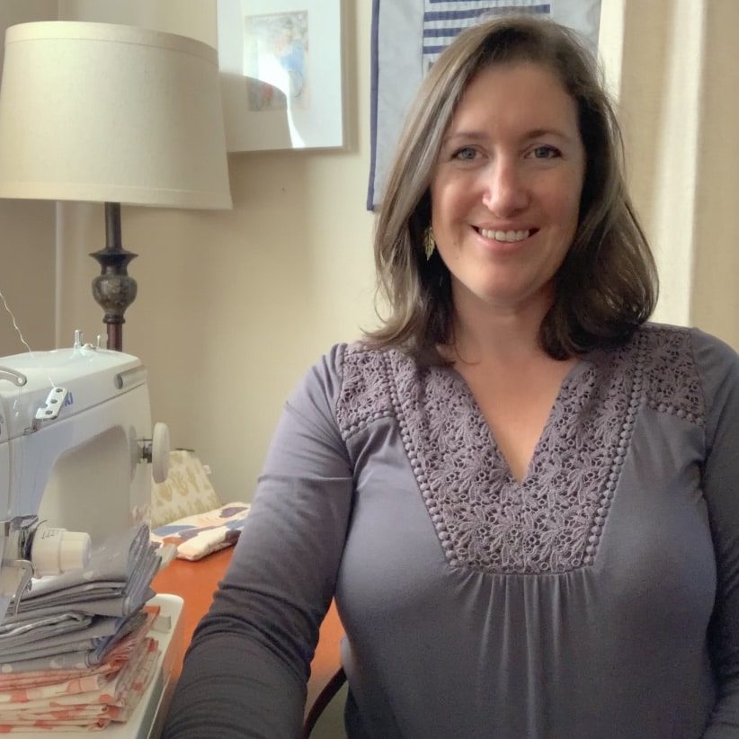 A woman smiling in front of a sewing machine.