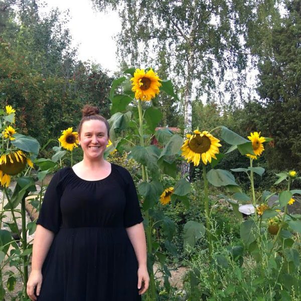 A woman in a black dress standing in front of sunflowers.