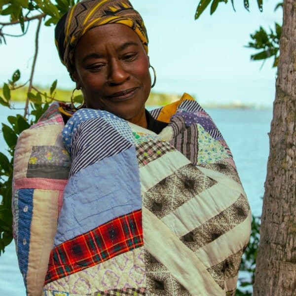 A woman wrapped in a blanket by the water.