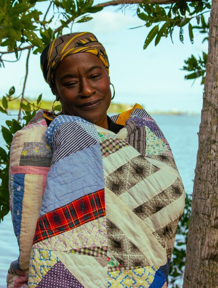 A woman wrapped in a blanket by the water.