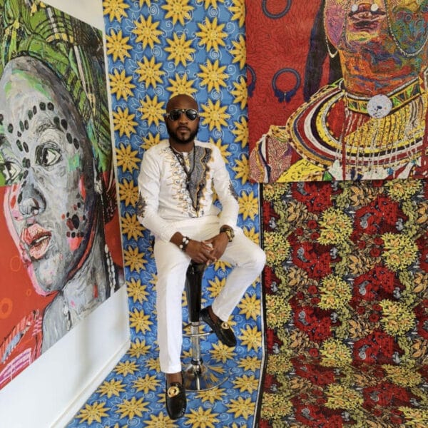 A man sitting on a stool in front of paintings.