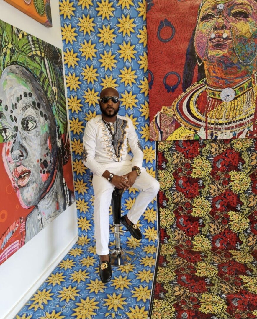 A man sitting on a stool in front of paintings.