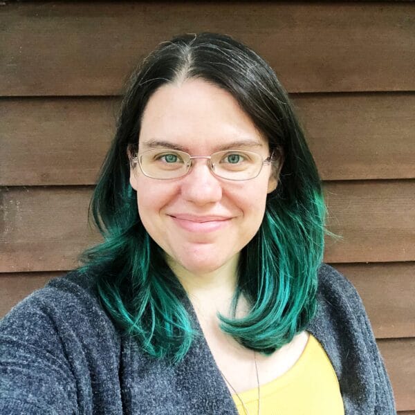 A woman with green hair in front of a wooden wall.