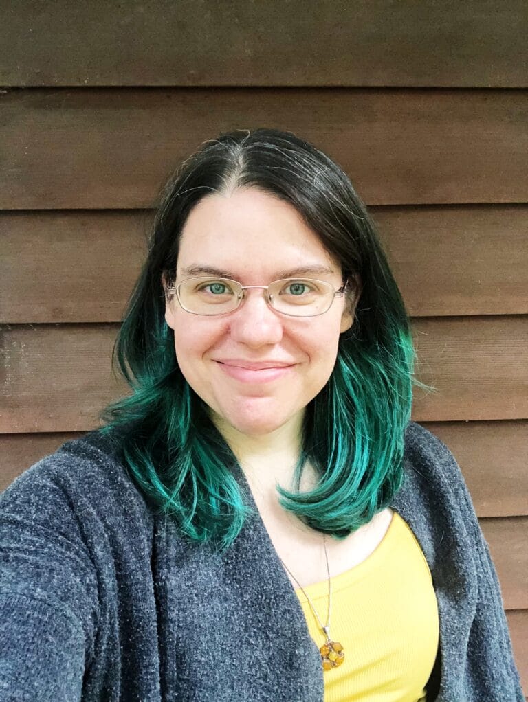 A woman with green hair in front of a wooden wall.