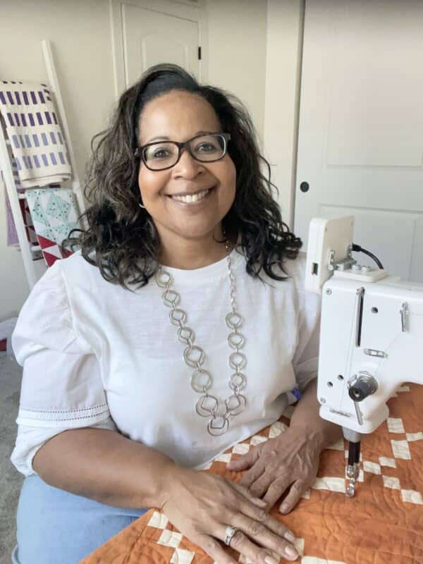 A woman is smiling while sitting in front of a sewing machine.