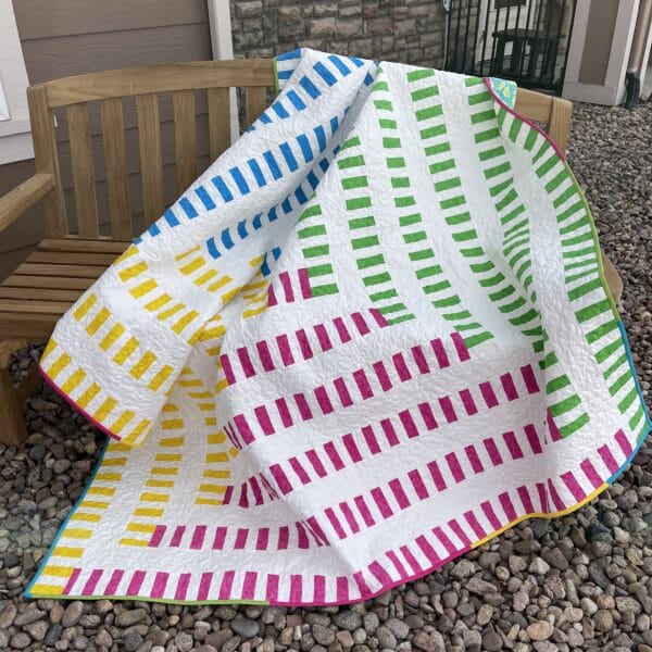 A colorful quilt sitting on a bench in front of a house.