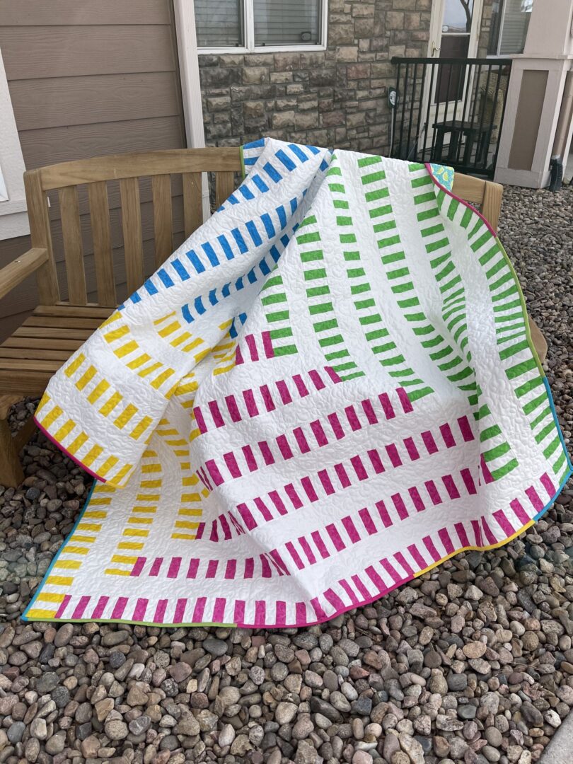 A colorful quilt sitting on a bench in front of a house.
