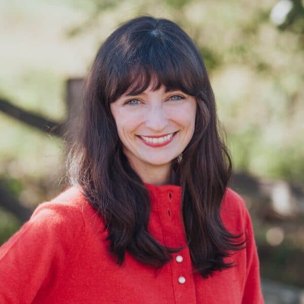 A woman in a red sweater smiles in front of a fence.