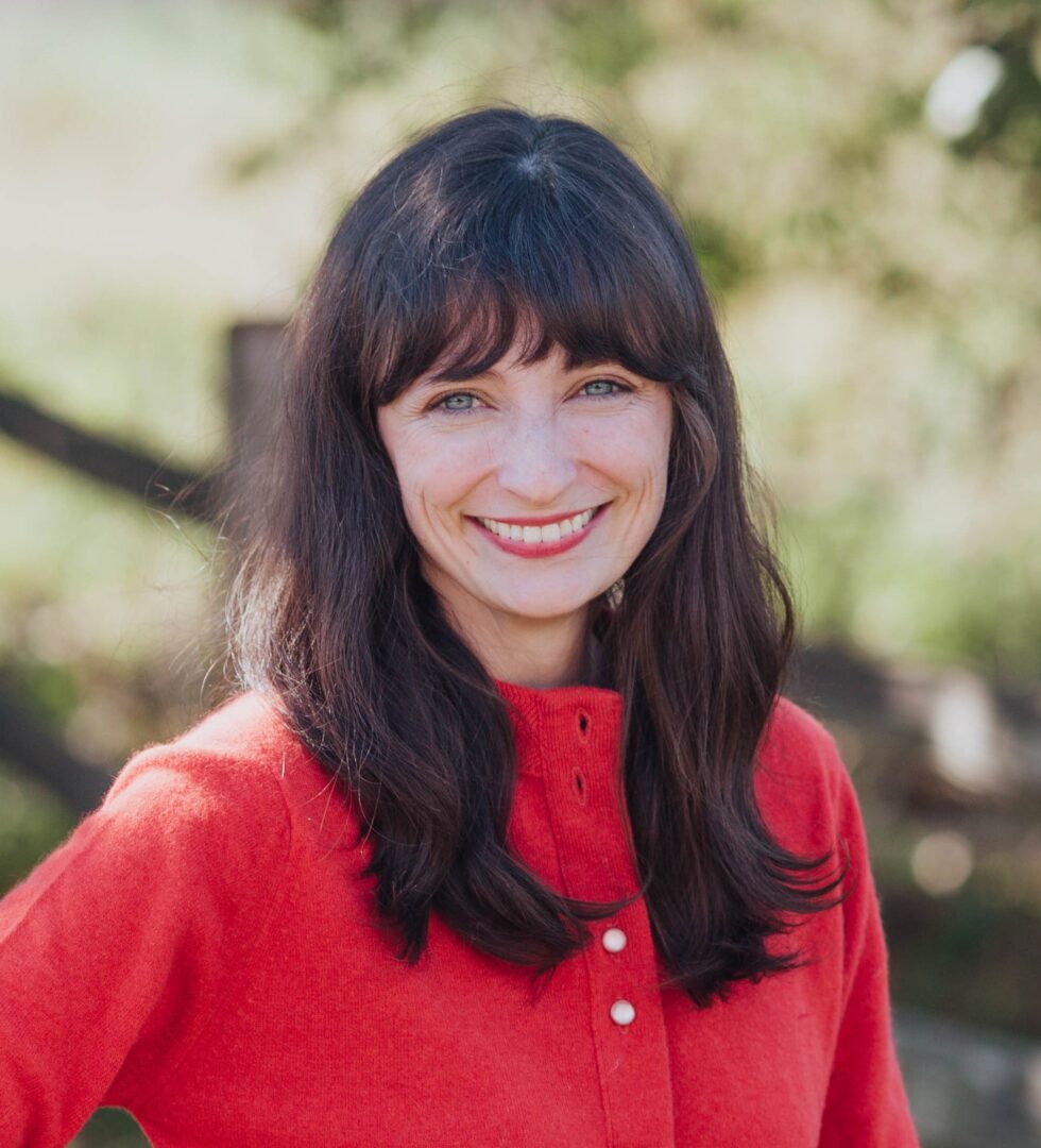 A woman in a red sweater smiles in front of a fence.