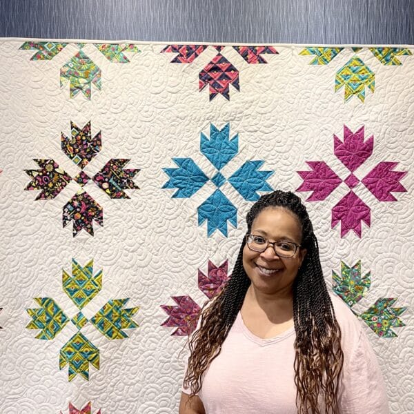 A woman standing in front of a colorful quilt.