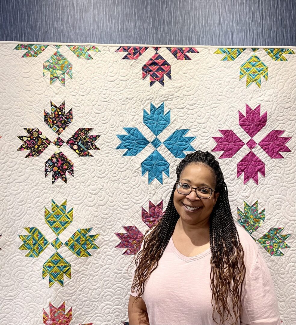 A woman standing in front of a colorful quilt.