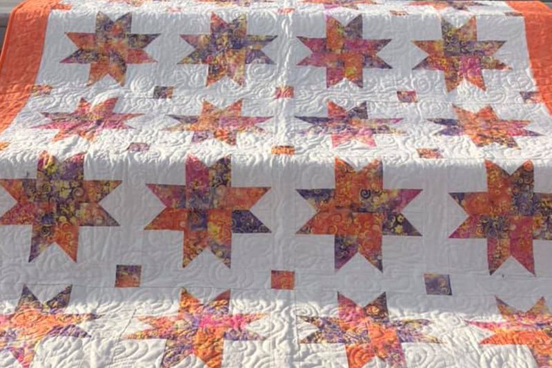 A quilt with orange and white stars on it.