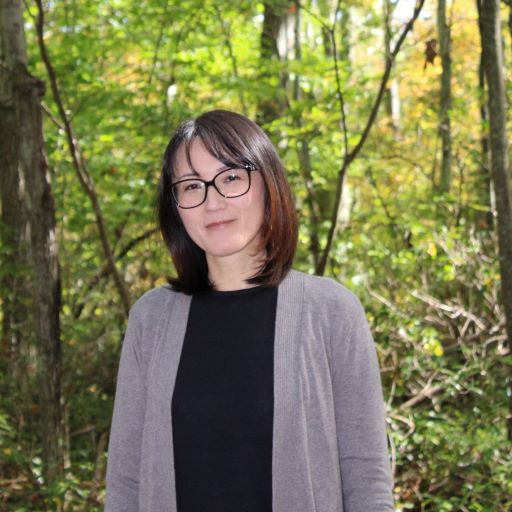 A woman in glasses standing in a wooded area.