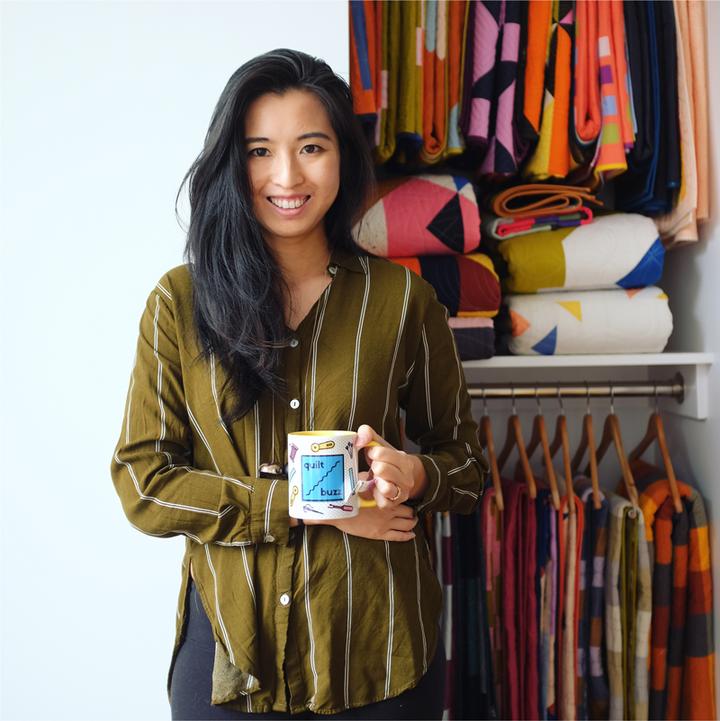 A woman holding a mug in front of a closet full of fabric.